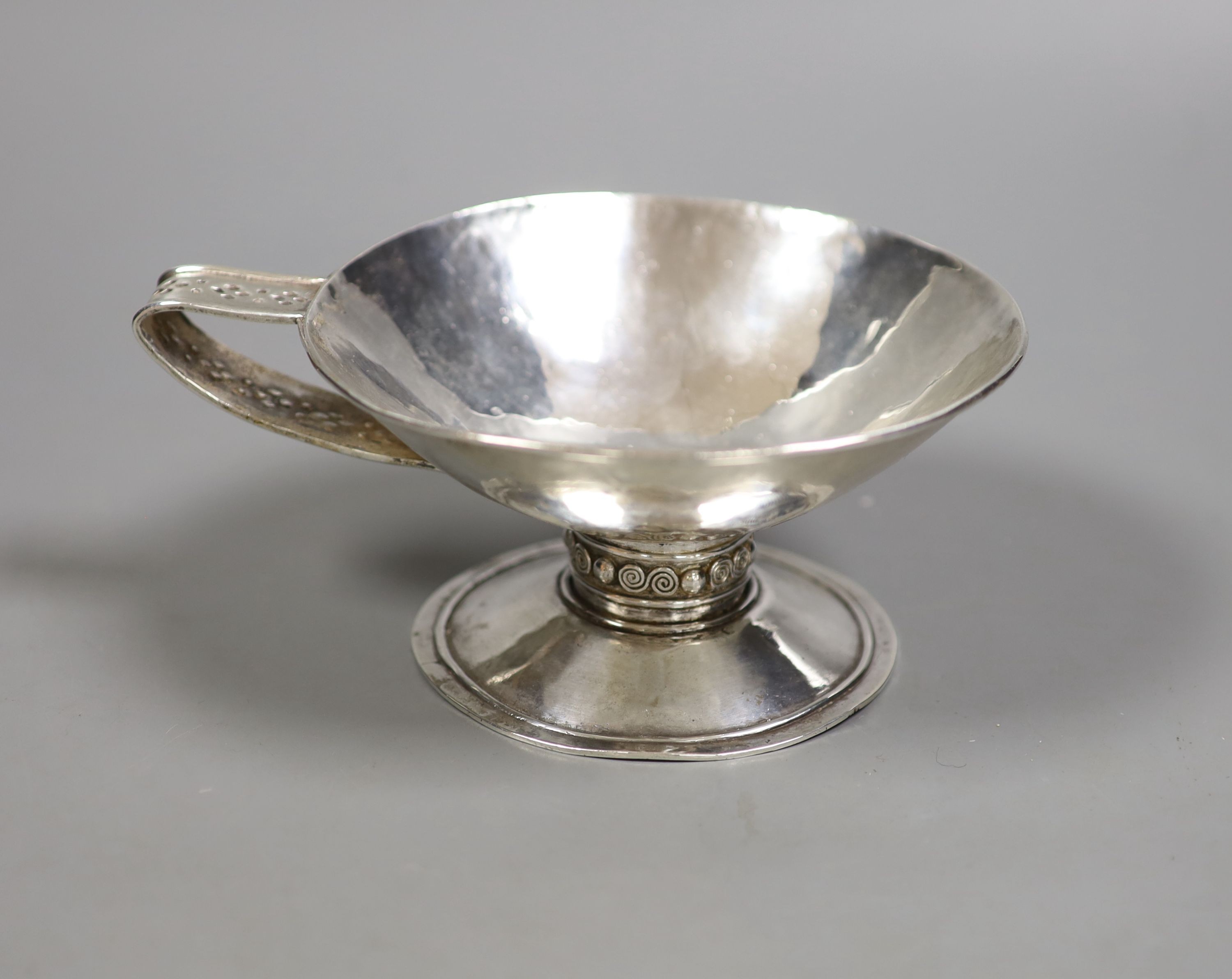 An Arts & Crafts planished white metal single handled pedestal cup, diameter 13.5cm, 6.5oz.